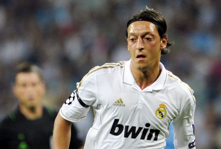 Camisa titular retrô Adidas do Real Madrid para a temporada 2011-12. A camisa branca e dourada apresenta o escudo do Real Madrid bordado no peito, o logotipo da Adidas nas mangas e ombros, o patrocínio da Bwin na frente da camisa e o nome e número do jogador personalizáveis (opcional). 